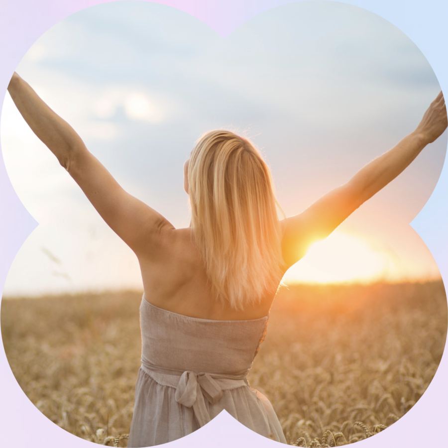A woman with arms raised toward the sunset in a wheat field